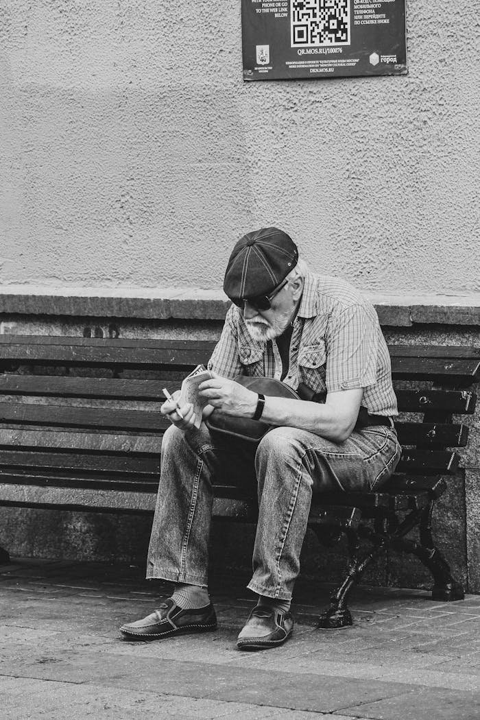 A senior man sits on a bench reading, captured in classic black and white street photography.