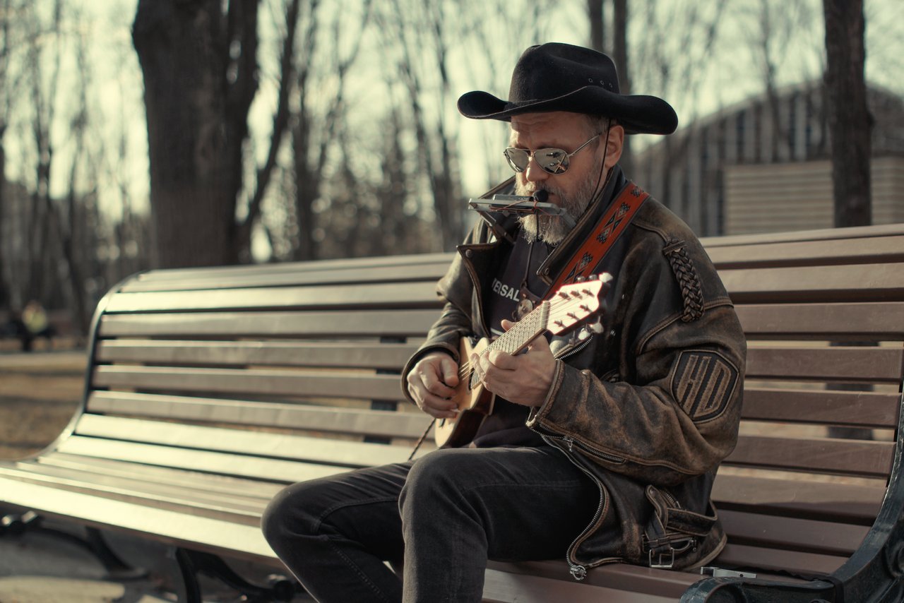 A street musician playing guitar and harmonica on a park bench in Kharkiv, Ukraine, during autumn.