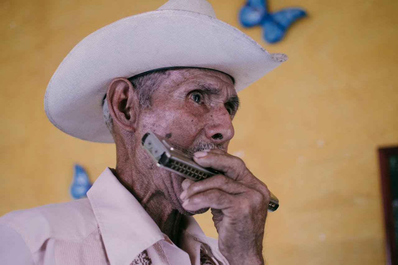 A senior man wearing a cowboy hat plays the harmonica against a colorful background in Mata de Jobo, Mexico.