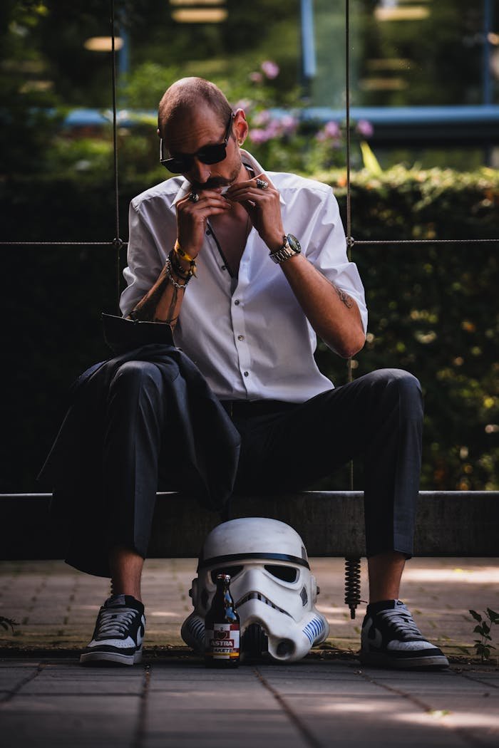 A stylish man in sunglasses and white shirt playing the harmonica outdoors, with helmet.