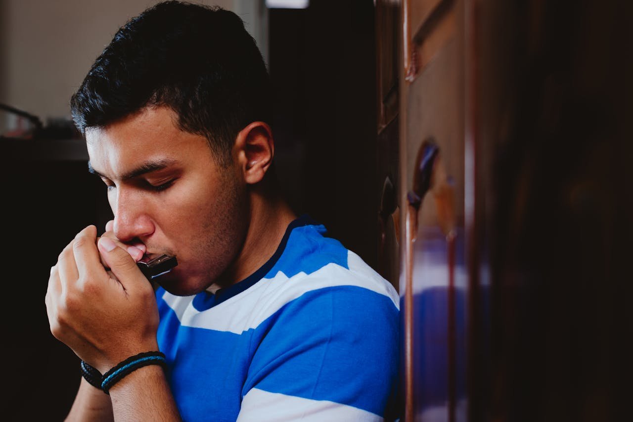 Close-up shot of a man indoors intently playing a harmonica in Juiz de Fora.